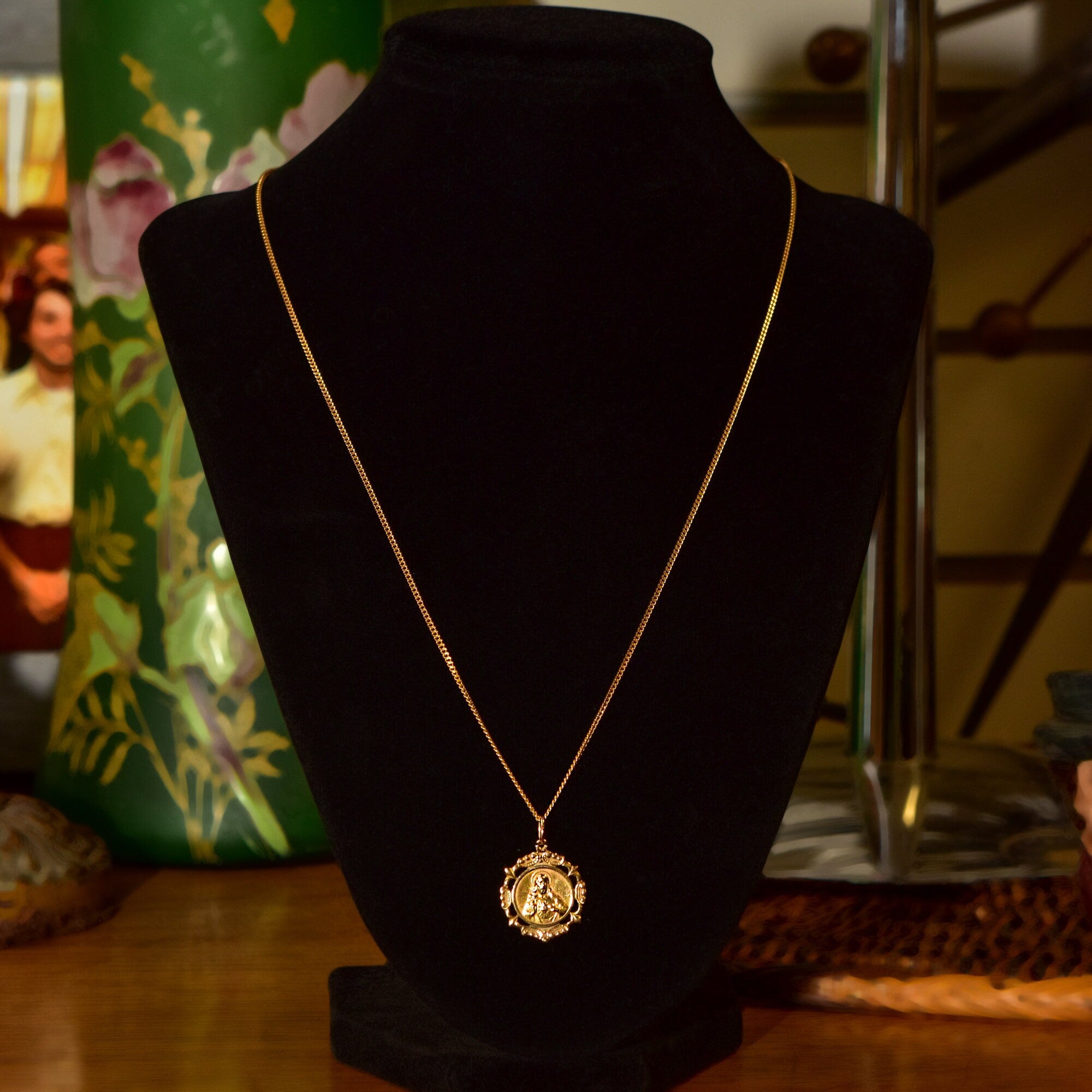18K yellow gold Sacred Heart of Jesus pendant necklace with embossed medallion on a delicate 1.5mm curb chain, religious jewelry displayed on a black velvet bust