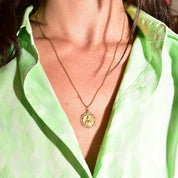 18K yellow gold Sacred Heart of Jesus pendant necklace with embossed medallion on a thin curb chain, worn by a person in a green striped shirt.