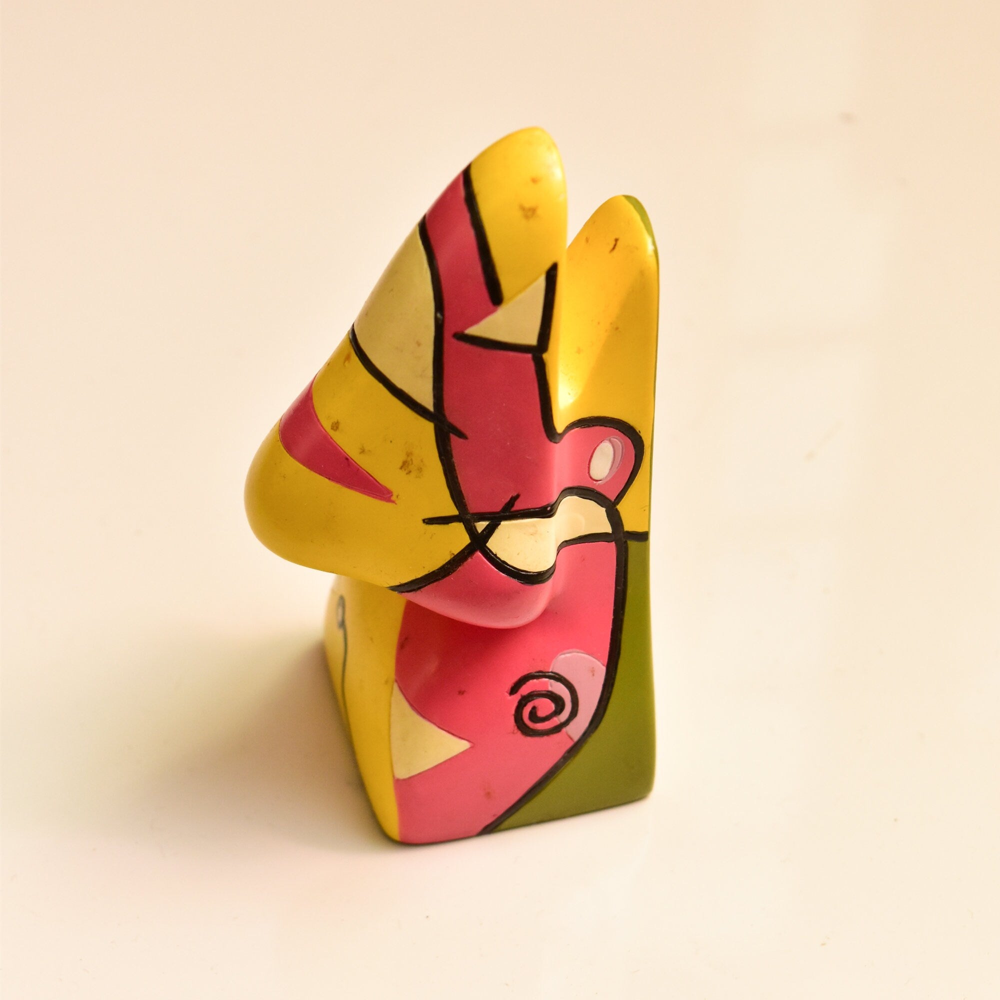 Colorful abstract resin eyeglass holder in the style of Picasso, featuring yellow, red and green geometric shapes resembling a face, measuring 3 3/4 inches high, vintage home decor accessory.