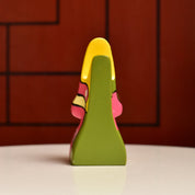 Colorful abstract resin eyeglass holder stand shaped like a face with yellow, green and pink tones against a red brick background, measuring 3 3/4 inches tall, vintage home decor accent piece