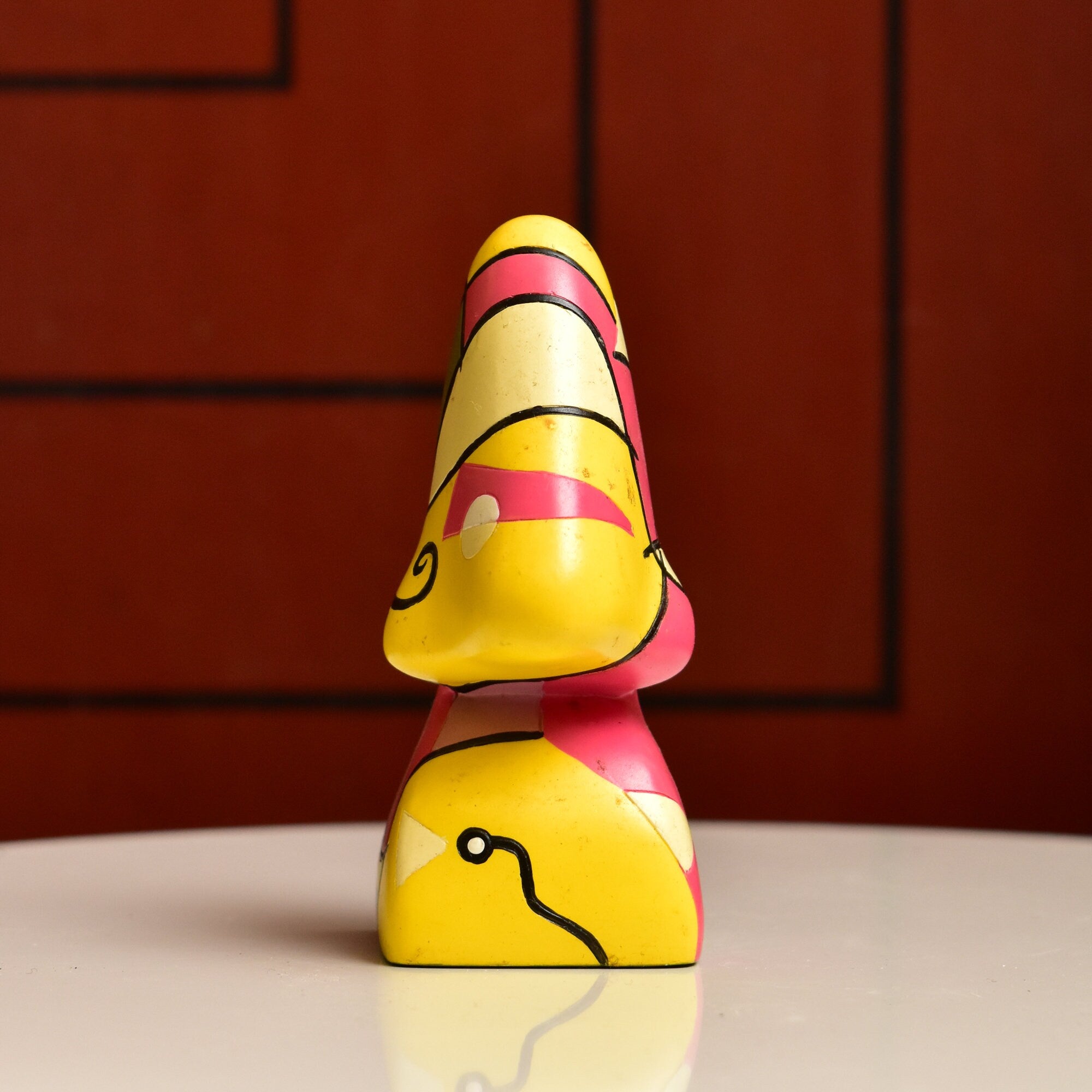 Colorful abstract resin eyeglass stand shaped like a face with distinct geometric features in yellow, pink and black against a red background, measuring 3 3/4 inches tall, vintage home decor accessory.