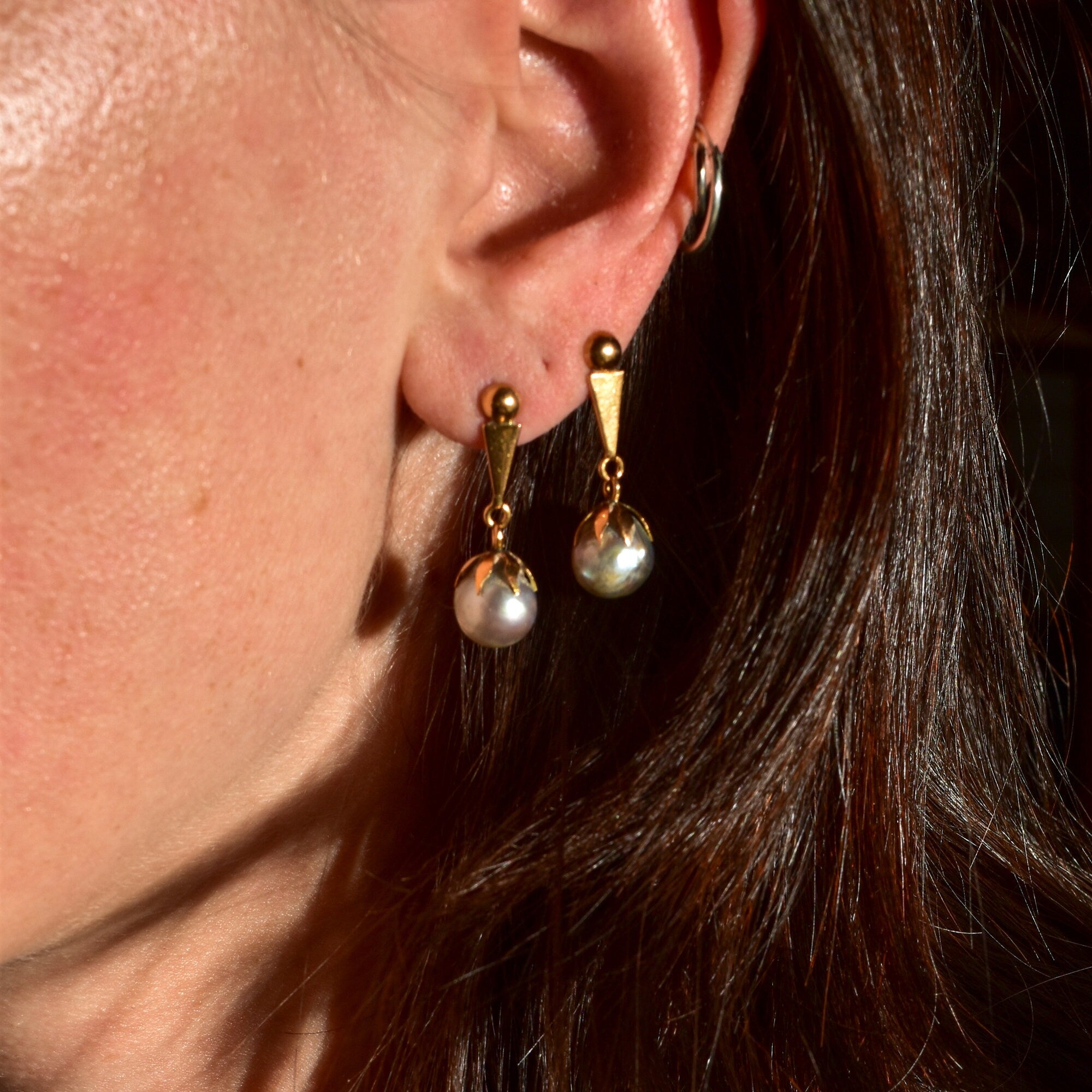 18K yellow gold baroque freshwater pearl dangle earrings on a model's ear, showing the elegant drop design against dark hair.
