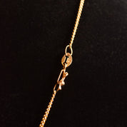 18K yellow gold Sacred Heart Jesus pendant necklace with embossed medallion on thin curb chain, religious jewelry closeup on black background