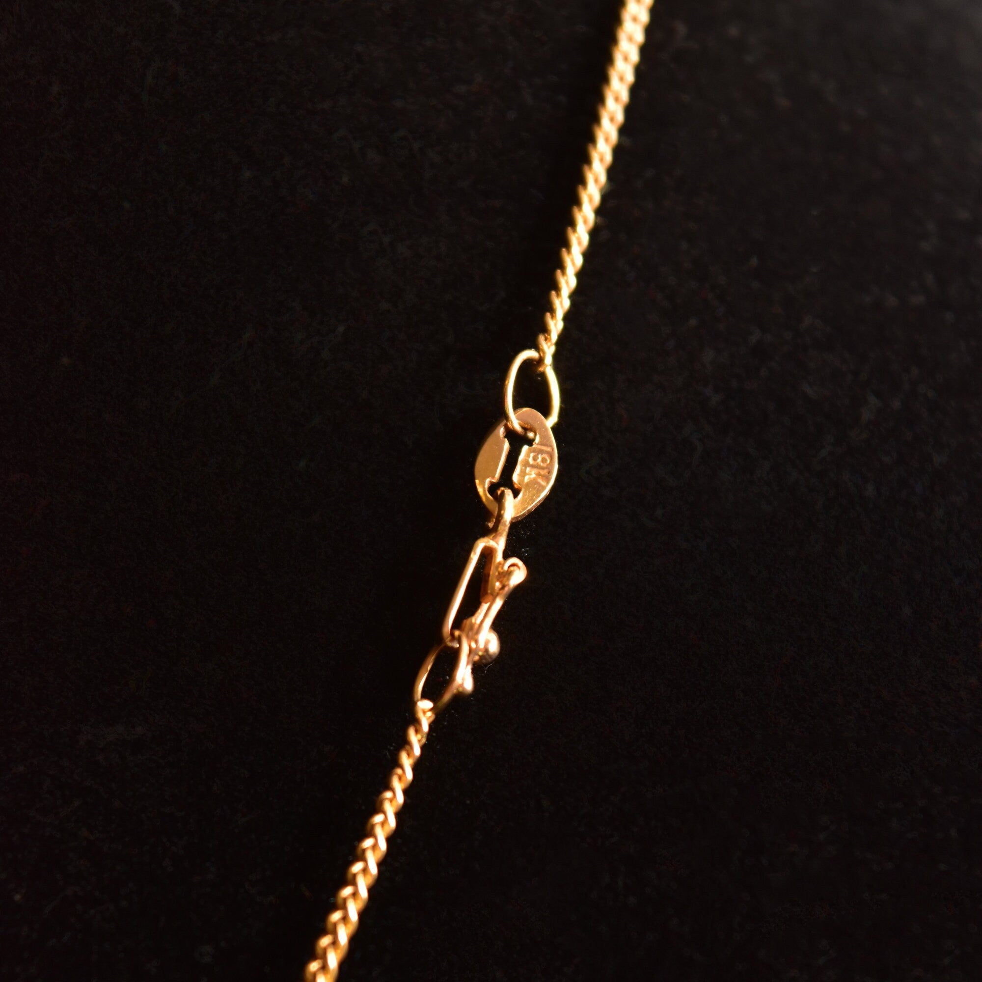 18K yellow gold Sacred Heart Jesus pendant necklace with embossed medallion on thin curb chain, religious jewelry closeup on black background