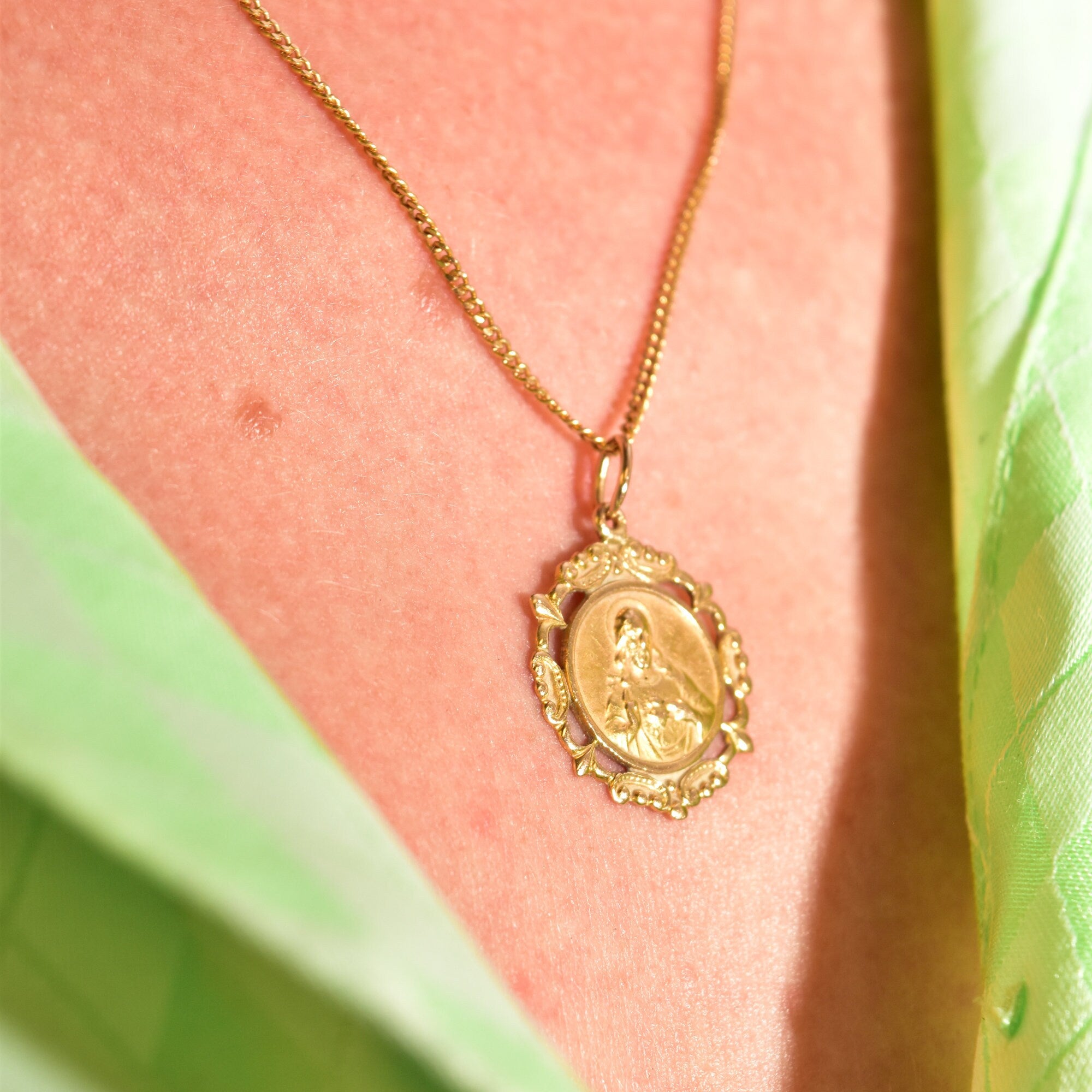 18K gold Jesus Sacred Heart pendant necklace on woman's chest, yellow gold embossed medallion on thin gold chain, religious jewelry close-up