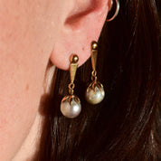 Close-up of a woman's ear wearing elegant 18K yellow gold dangle earrings featuring baroque freshwater pearls measuring approximately 29mm. The earrings have original push-back closures and are estate jewelry pieces.