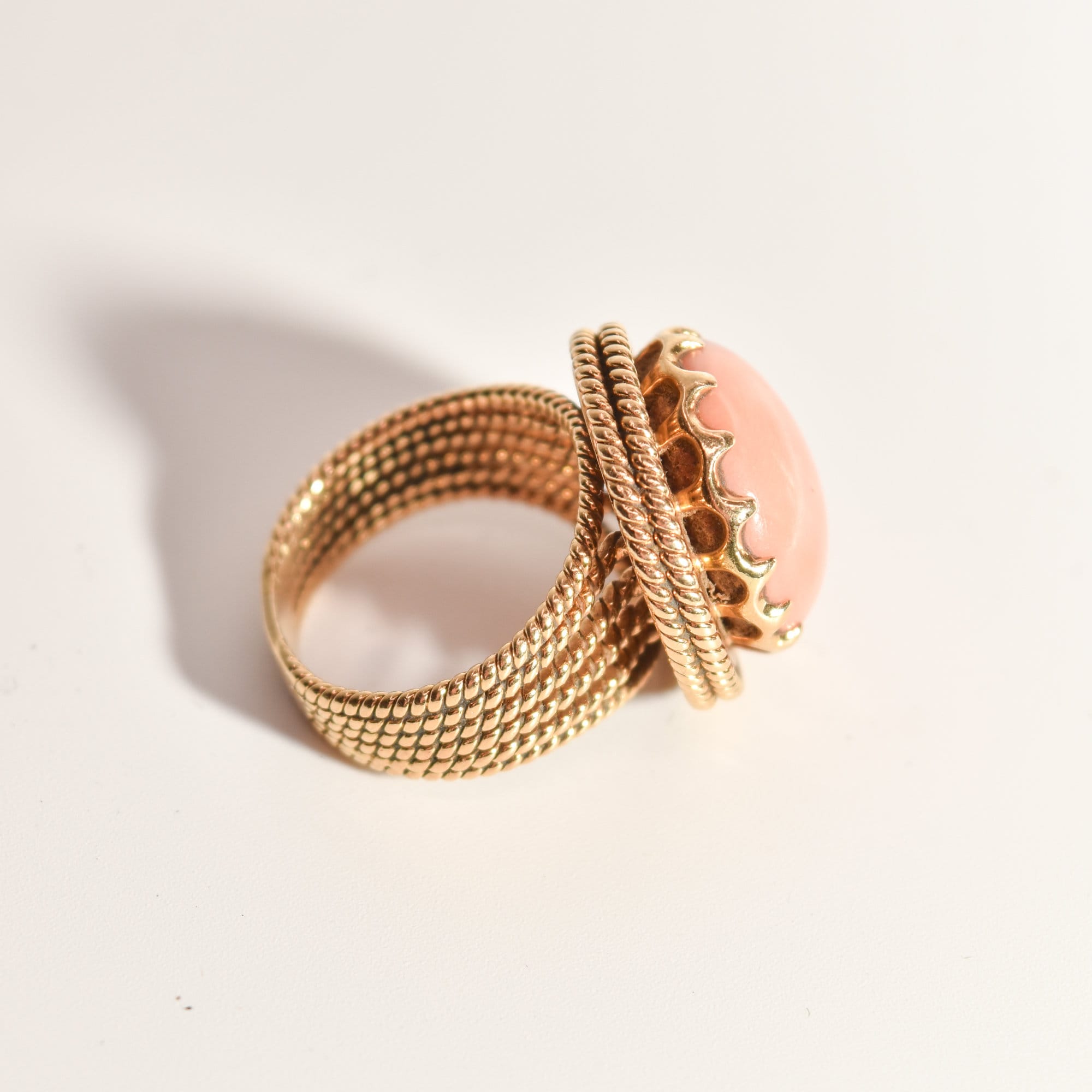 Estate angel skin coral cocktail ring in 18K yellow gold with woven gold band, size 6.25 US, on white background.