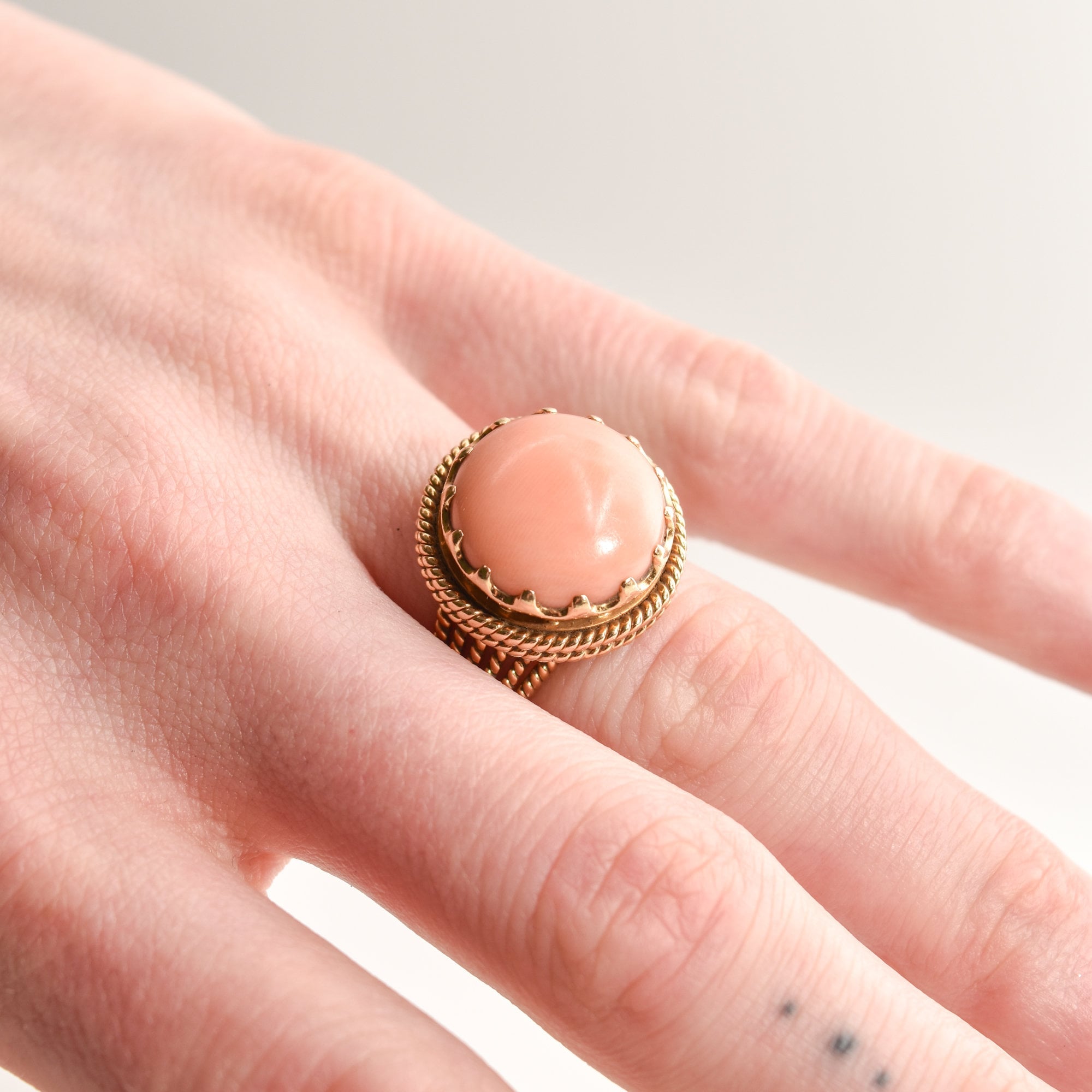 Estate Angel Skin Coral Cocktail Ring in 18K Yellow Gold on a finger, featuring a woven gold band, size 6.25 US, against a white background.